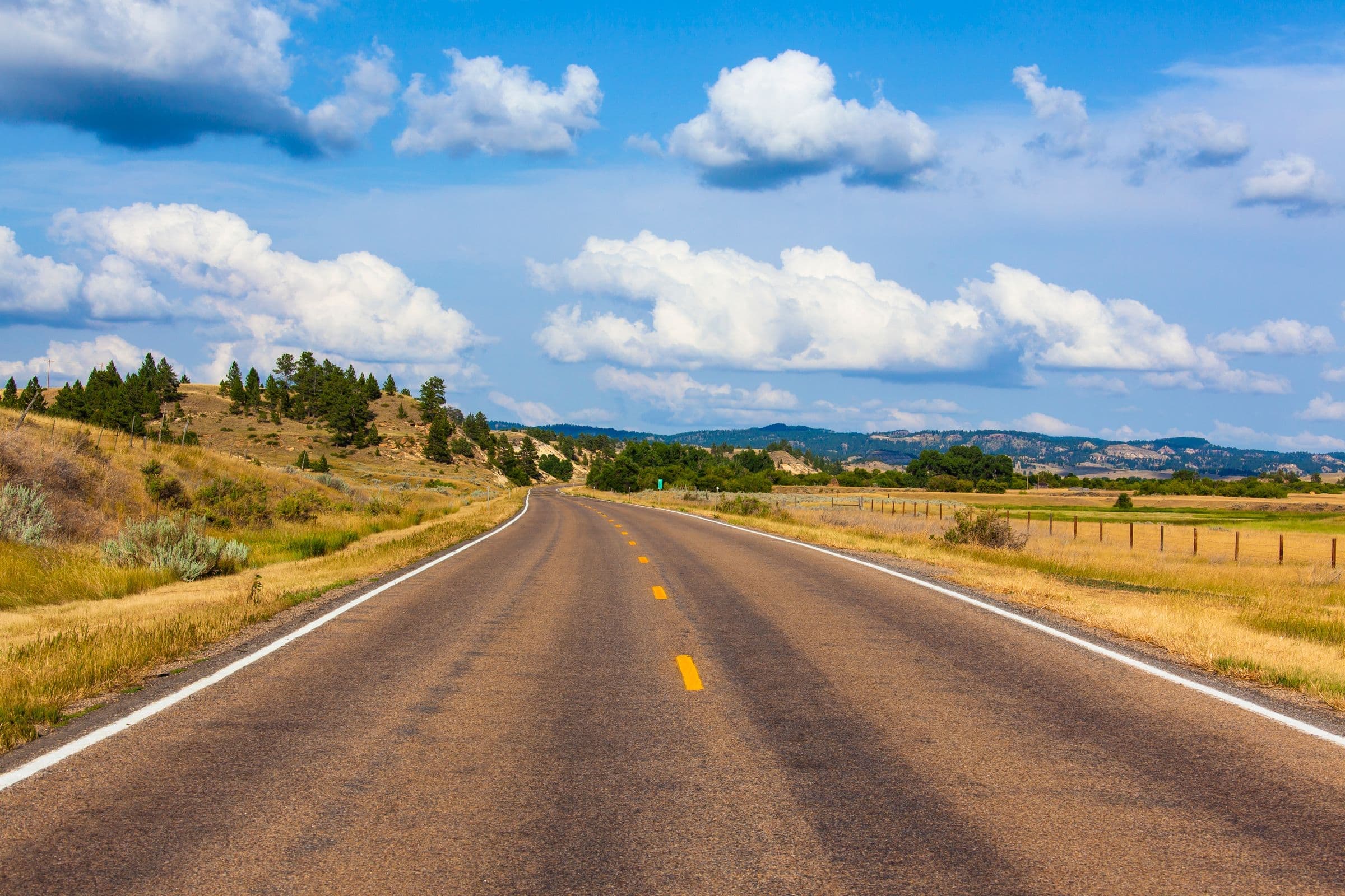 Two-lane Montana highway through rolling grassland under big clouds