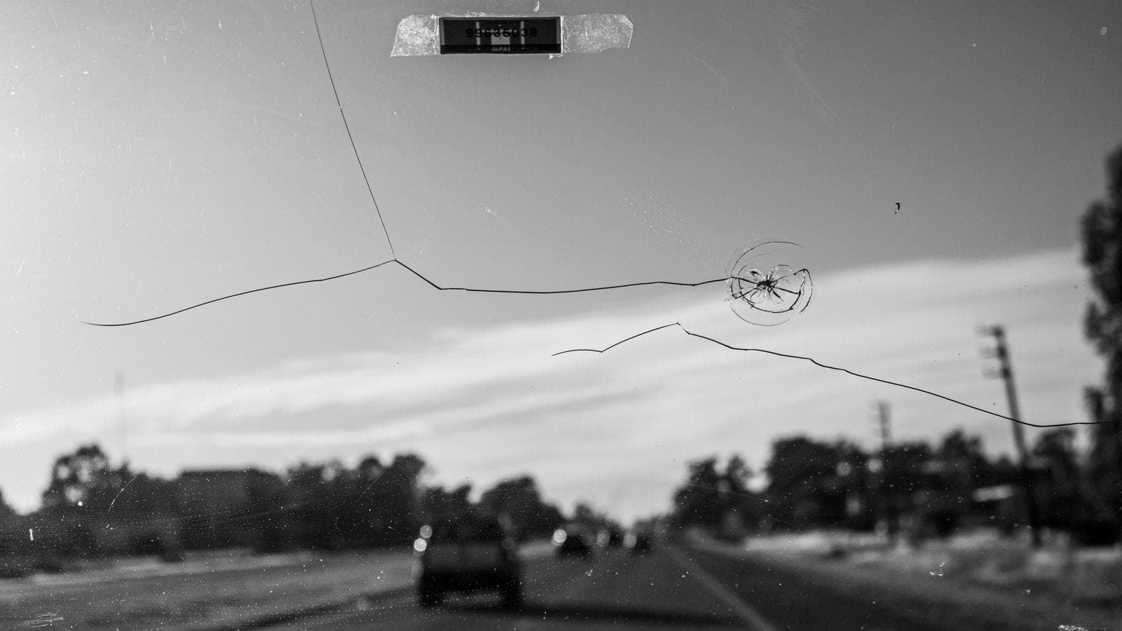 Long crack and impact point across a windshield on a highway drive