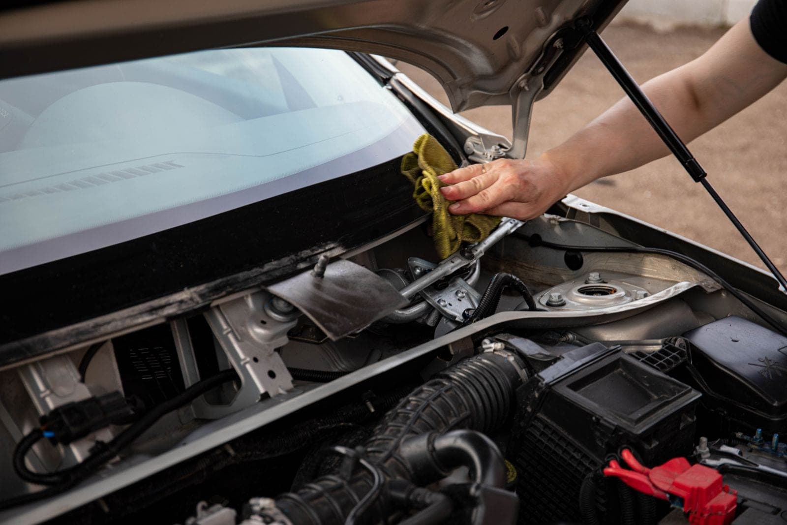 Technician wiping down the base of a windshield with the hood open
