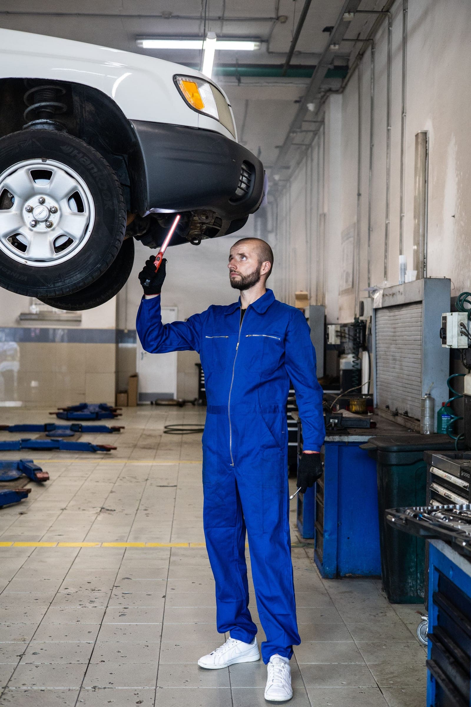 Technician in coveralls working under a raised vehicle in a repair shop