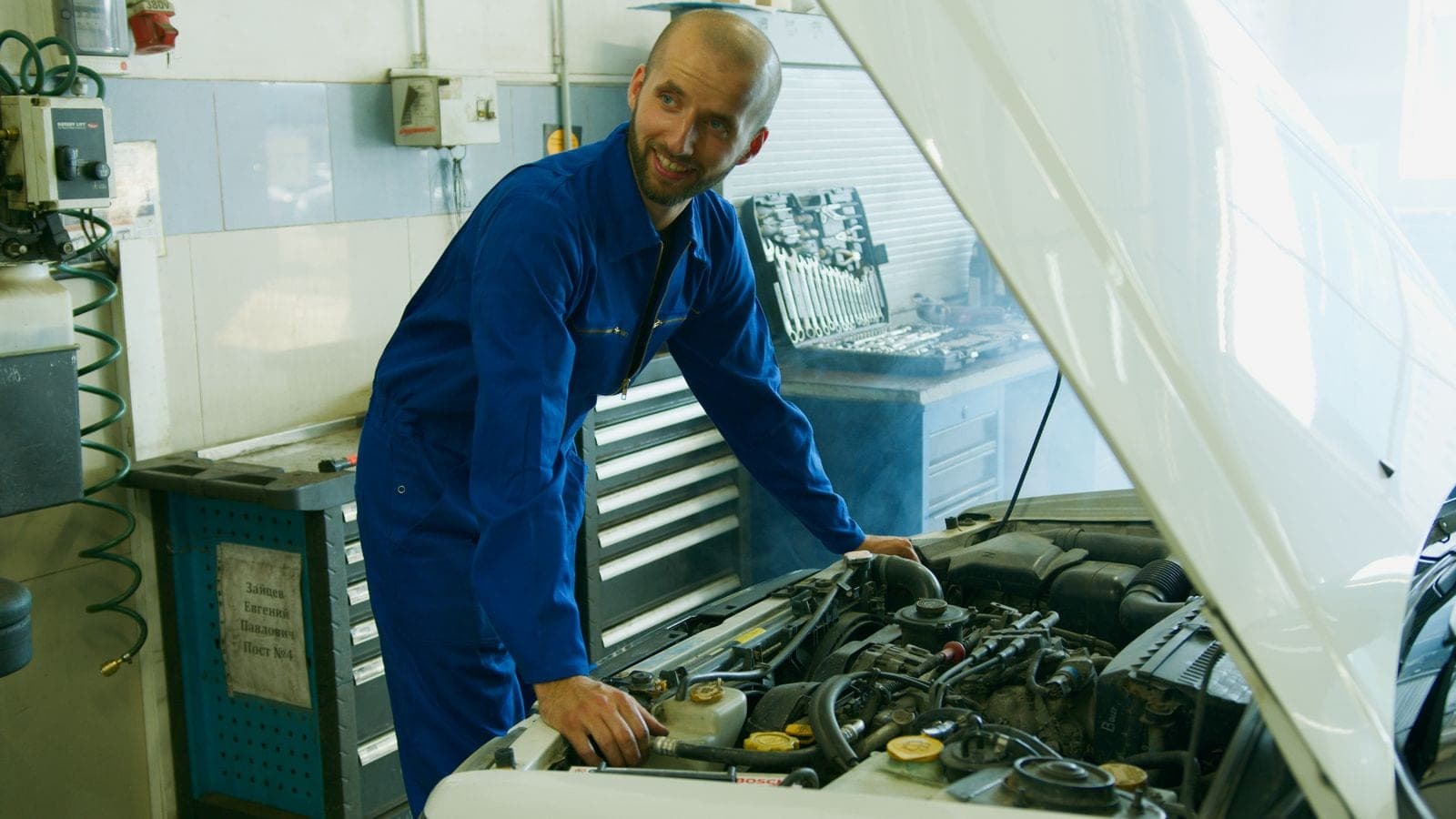 Smiling technician in coveralls working in a tidy shop
